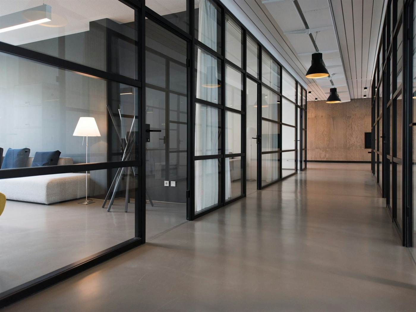 A glass-walled office corridor with a seating room visible through the windows
