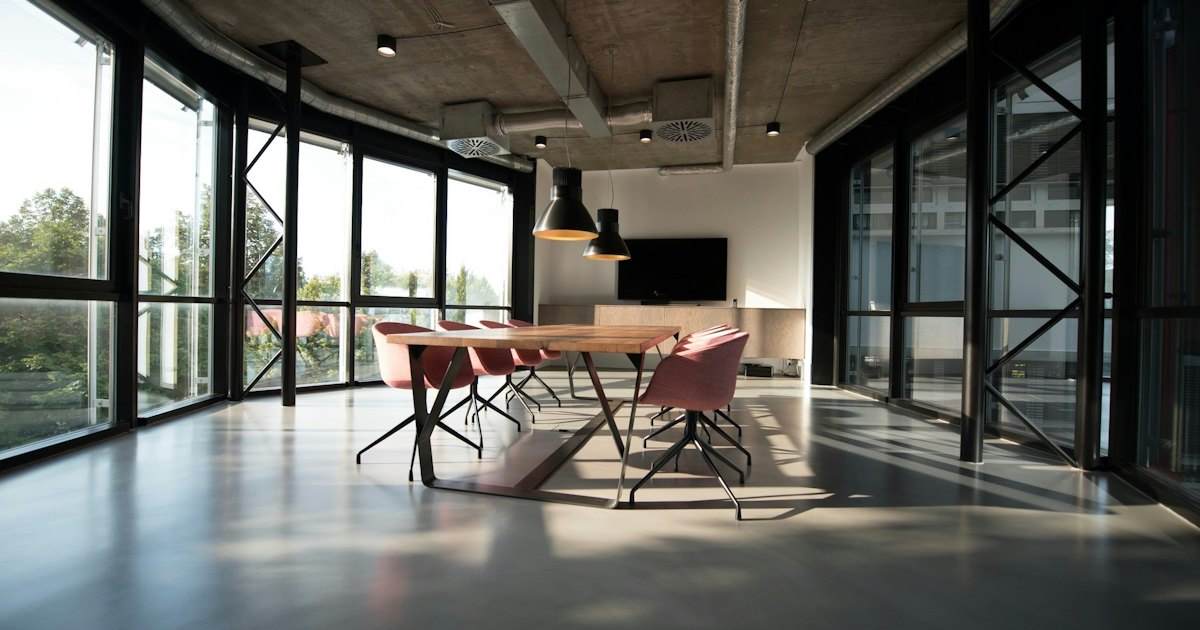 An empty meeting room with a wooden table, chairs, and tall windows